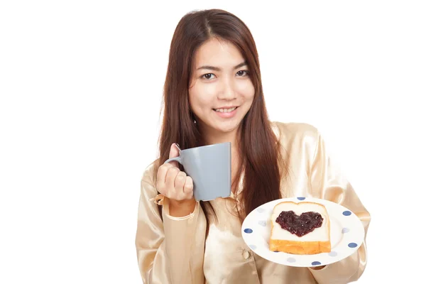 Asiatin im Schlafanzug mit Kaffee und herzförmiger Marmelade auf Brot — Stockfoto