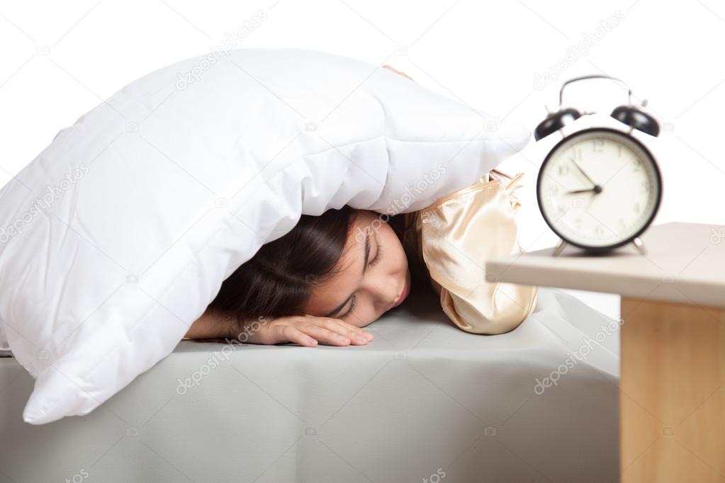 Sleepy Asian girl use pillow cover ears and alarm clock