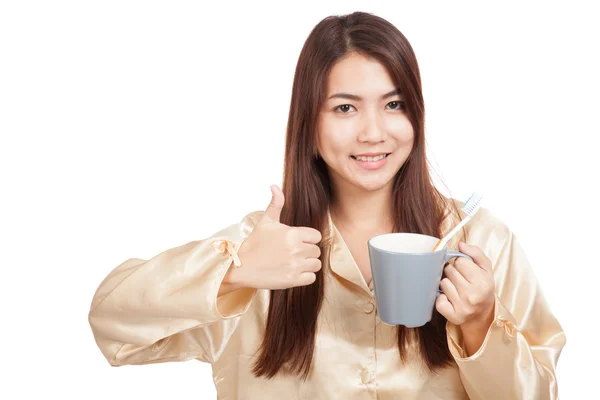 Asian woman in pajamas thumbs up with toothbrush in mug — Stock Photo, Image