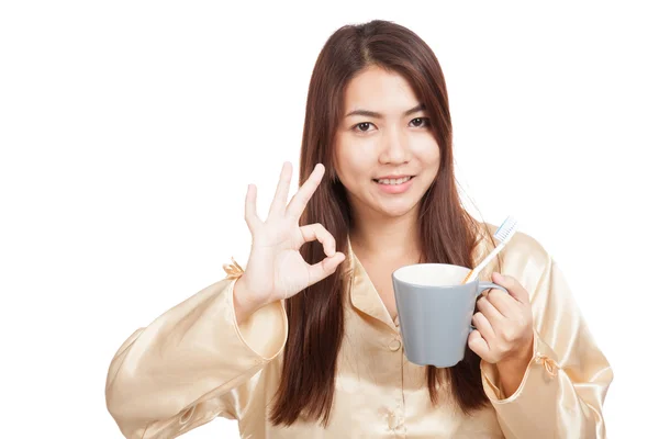 Asian woman in pajamas show OK with toothbrush in mug — Stock Photo, Image