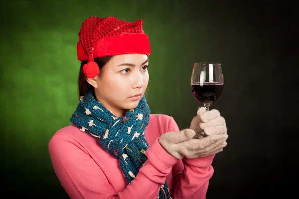 Asiática chica con rojo navidad sombrero mira en vaso de vino — Foto de Stock