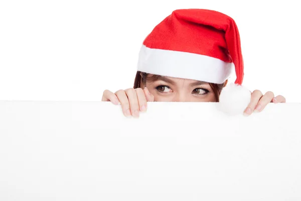 Asian girl with red santa hat peeking behind a blank board — Stock Photo, Image