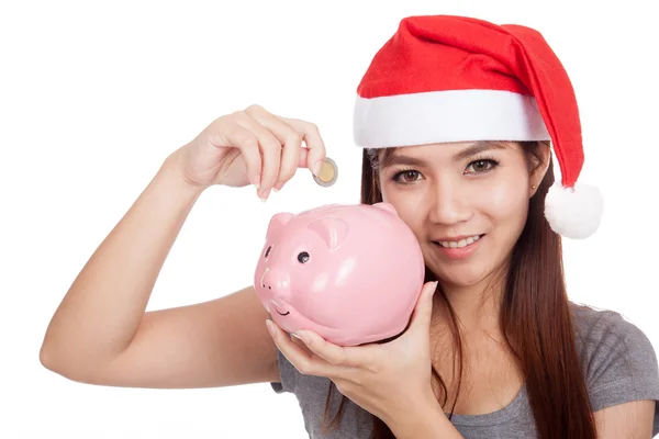 Asian girl with red santa hat put a coin to pink piggy bank — Stock Photo, Image