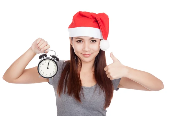 亚洲女孩与红色圣诞老人帽子竖起大拇指与闹钟 — 图库照片
