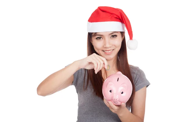 Asian girl with red santa hat put a coin to pink piggy bank Stock Photo