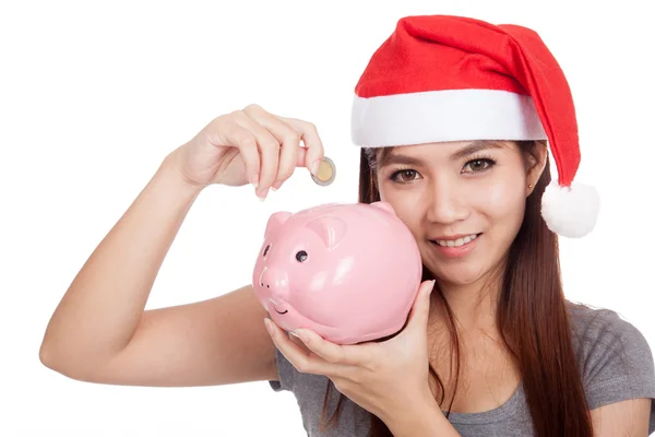 Asian girl with red santa hat put a coin to pink piggy bank Royalty Free Stock Photos