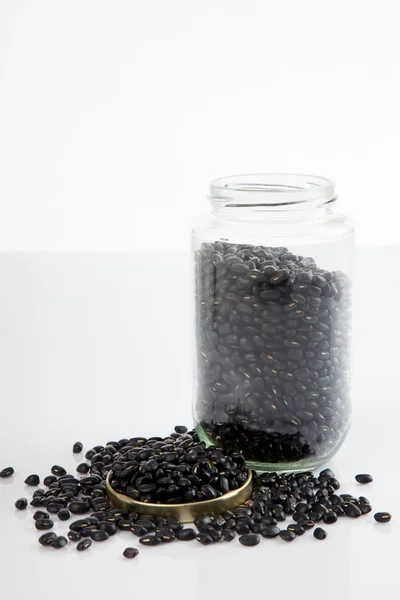 Schwarze Bohnen im Glas auf weißem Tisch mit Deckel — Stockfoto