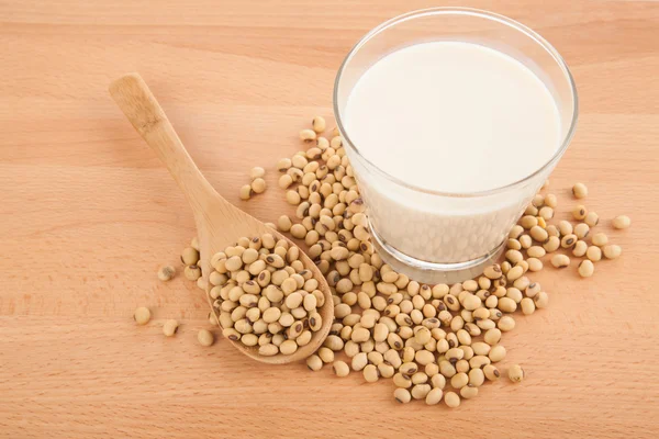 Soy milk in glass with soybeans and wooden spoon — Stock Photo, Image