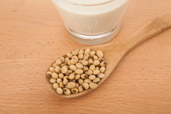 Soy milk in glass with soybeans and wooden spoon — Stock Photo, Image