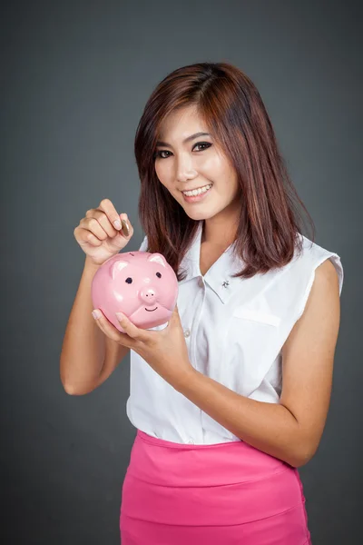 Schöne asiatische Mädchen setzen eine Münze zu rosa Schwein Spardose — Stockfoto