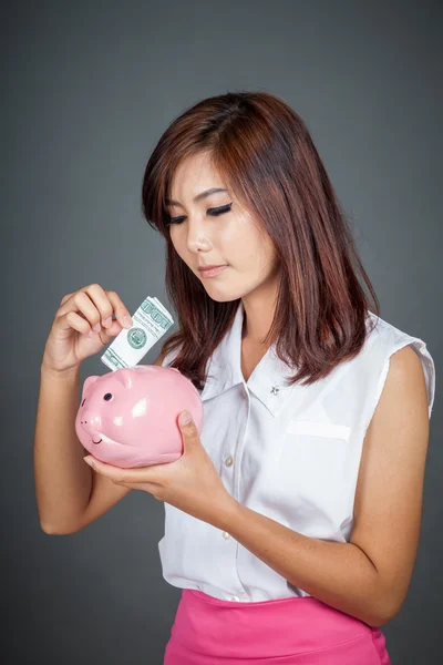 Beautiful Asian girl put a bill to pink pig money box — Stock Photo, Image