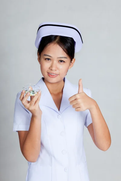 Young Asian nurse show thumbs up with some pills — Stock Photo, Image