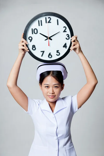 Jeune infirmière asiatique montrer une horloge sur sa tête — Photo