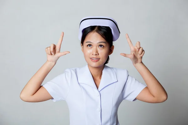 Junge asiatische Krankenschwester zeigen mit beiden Händen nach oben und schauen nach oben — Stockfoto