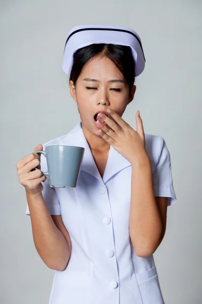 Unga asiatiska sjuksköterska gäspning med en kopp kaffe — Stockfoto