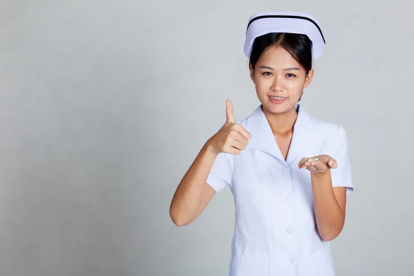 Asiática joven enfermera thumbs arriba con píldoras en su palma mano — Foto de Stock