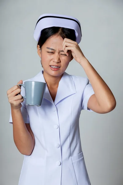 Jovem enfermeira asiática tem dor de cabeça com uma xícara de café — Fotografia de Stock