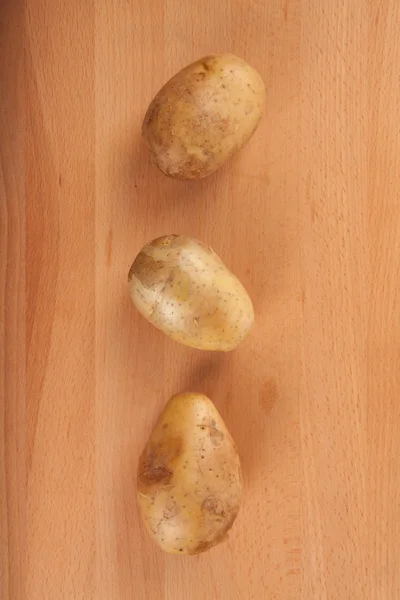 Three potatoes on wooden table — Stock Photo, Image