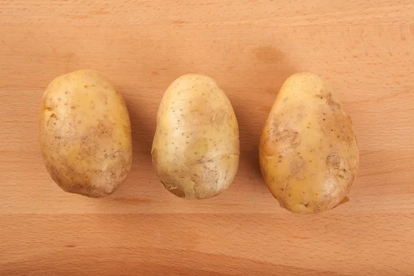 Three potatoes on wooden table — Stock Photo, Image