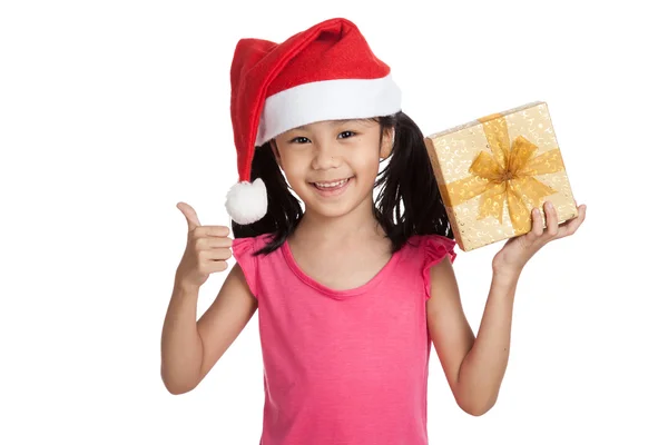 Piccola ragazza asiatica con Babbo Natale cappello e scatola regalo pollici in su Fotografia Stock