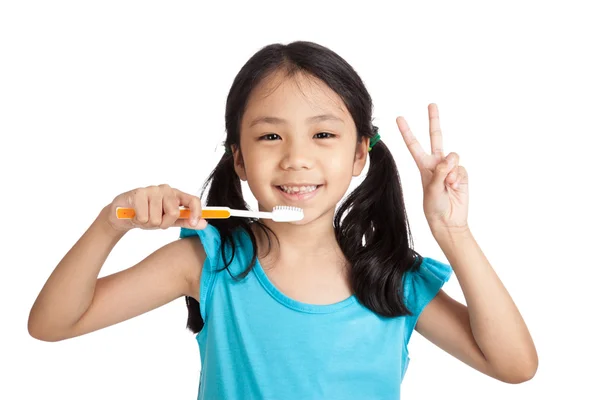 Pequeña chica asiática mostrar señal de victoria con cepillo de dientes —  Fotos de Stock