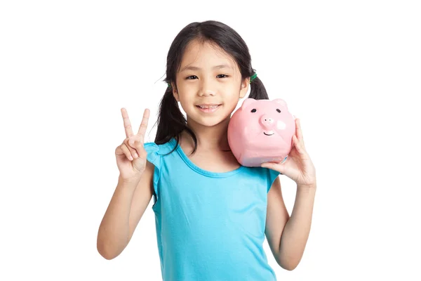 Little asian girl show victory sign with piggy bank — Stock Photo, Image