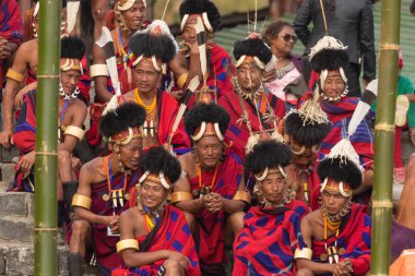 Selective focus image of Naga tribesmen wearing their traditional attire and siting together in Kisama Village arena in Nagaland India on 4 December 2016 clipart