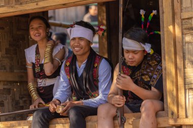 3 Aralık 2016 'da Hindistan' ın Nagaland kentindeki Kisama Heritage köyünde geleneksel giysiler içinde oturan genç Naga oğlanları ve bir Naga kızının seçici odak noktası.
