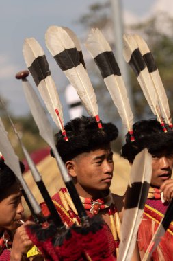 3 Aralık 2016 'da Hindistan' ın Nagaland kentindeki Kisama Heritage köyünde renkli giysiler içinde oturan ve baş vitesli genç Naga 'nın seçici odak görüntüsü