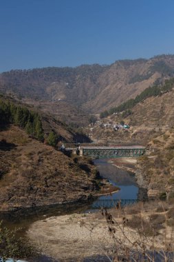 12 Ocak 2021 'de Uttara Khand Hindistan' ın Kumaun bölgesinde, üzerinde kayalık dağlar ve bir köprü bulunan dar bir vadiden akan bir nehrin görüntüsü.