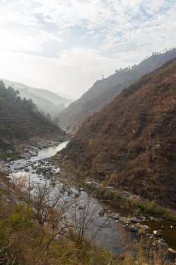 Dar bir vadiden akan bir nehrin manzarası. Ufukta bulutlar ve mavi gökyüzü ile dağılmış taşlar ve kayalar.