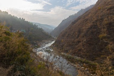 Dar bir vadiden akan bir nehrin manzarası. Ufukta bulutlar ve mavi gökyüzü ile dağılmış taşlar ve kayalar.