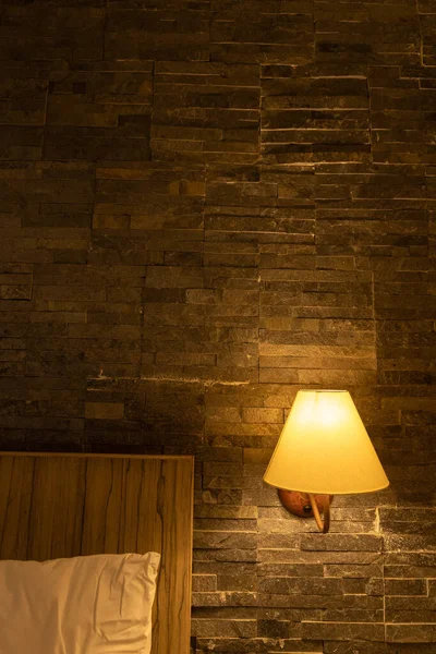 A bedside lamp shade on the wall illuminating the bed with pillow