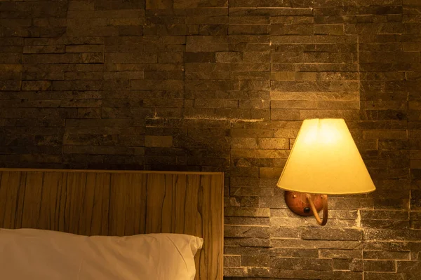 A bedside lamp shade on the wall illuminating the bed with pillow