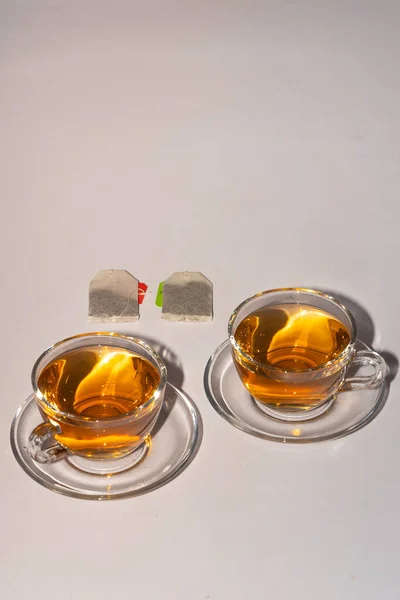 Two cups of black leaf tea in kept on a table with tea bags inside the cups and in background