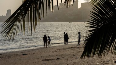 2 Nisan 2021 'de Mumbai Maharashtra Hindistan' daki Marine Drive plajında gün batımında insanların ve gökdelenlerin siluetleri.