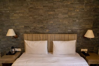 Yatak odasının içini beyaz çarşaflar, yatak odası ve yatak odası lambaları ve masalar düzgünce düzenlenmiş.