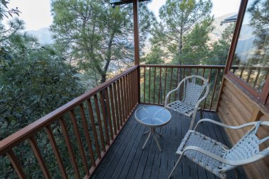 Manzaralı bir balkon manzarası, ahşap korkuluklar, rahat sandalyeler ve açık yeşil bir manzara. 
