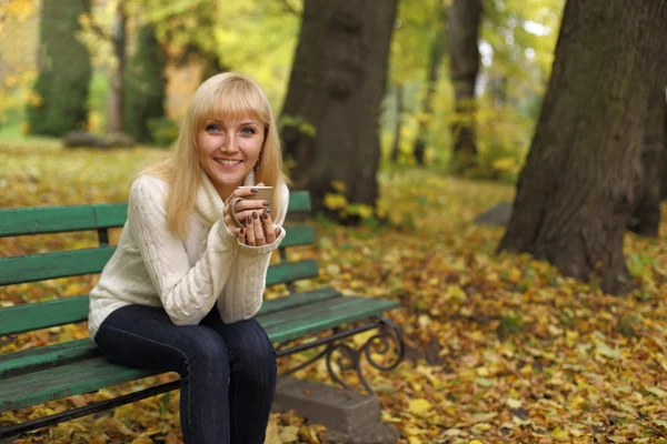 Chica con una taza de café en un banco en el parque en otoño —  Fotos de Stock