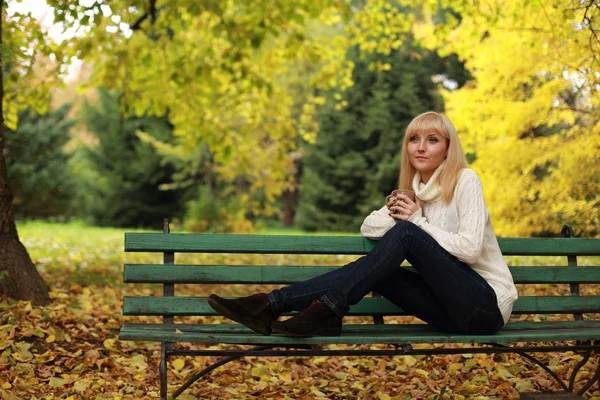 Ragazza con una tazza di caffè su una panchina nel parco in autunno — Foto Stock