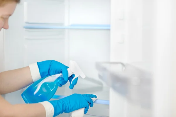 Beautiful woman cleans the refrigerator with a rag and soapy liq