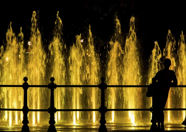 Mulher olhando para uma fonte colorida — Fotografia de Stock