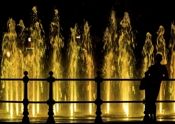 Frau blickt auf einen bunten Springbrunnen — Stockfoto