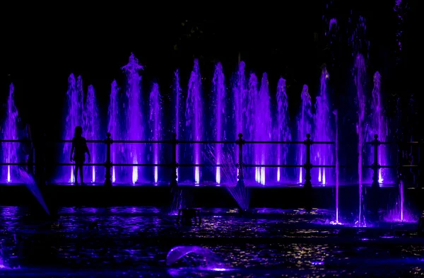 Kind blickt auf einen bunten Springbrunnen — Stockfoto