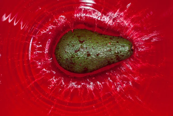 Zielony awokado w czerwonej wodzie — Zdjęcie stockowe