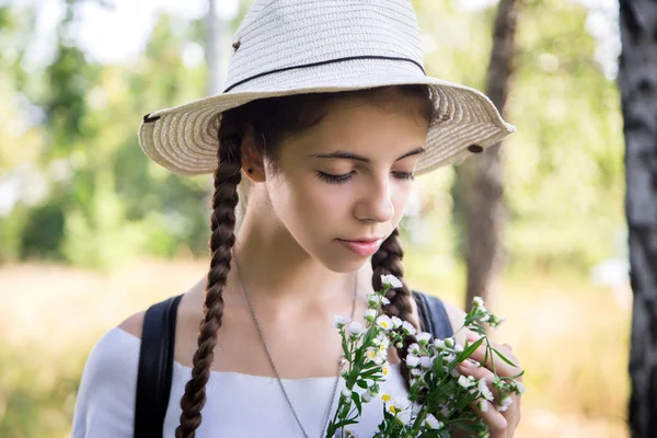 Hermosa chica en sombrero de paja con flores en sus manos, disfrutando de la naturaleza en un bosque de abedul — Foto de Stock