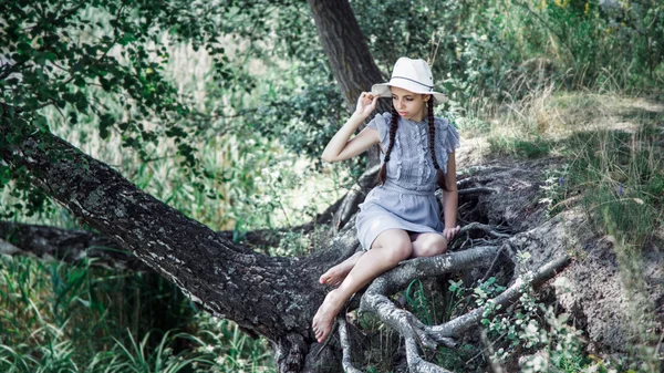 Giovane bella ragazza in cappello di paglia seduta sulla riva del lago. sorridente felice Foto Stock Royalty Free