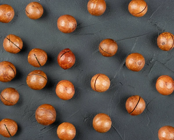 Spridda Makadamianötter Sina Skal Mörk Betong Bakgrund Ovanifrån — Stockfoto