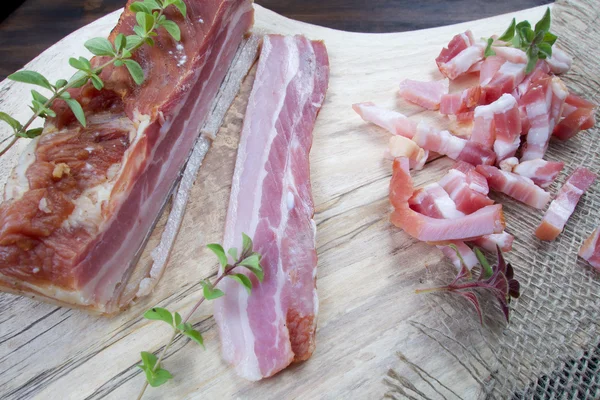 Bacon maison cru frais tranché sur des cubes sur une table en bois avec une herbe verte — Photo