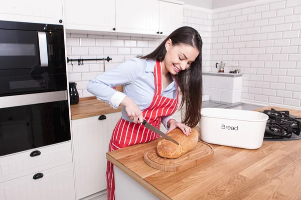 Ung kvinna skära bröd i köket. Stockbild